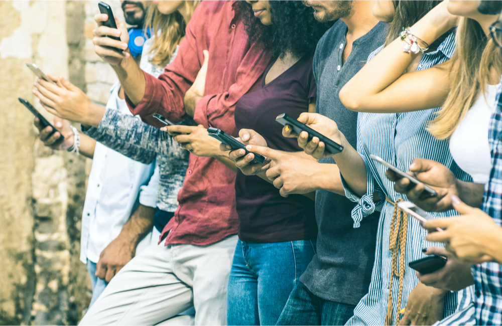 Group of co-workers sharing information on their phones to illustrate where content, community, and customer experience meet