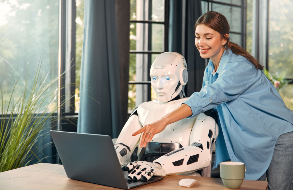 Woman collaborating with robot at laptop to illustrate techno-optimism combined with building a human brand